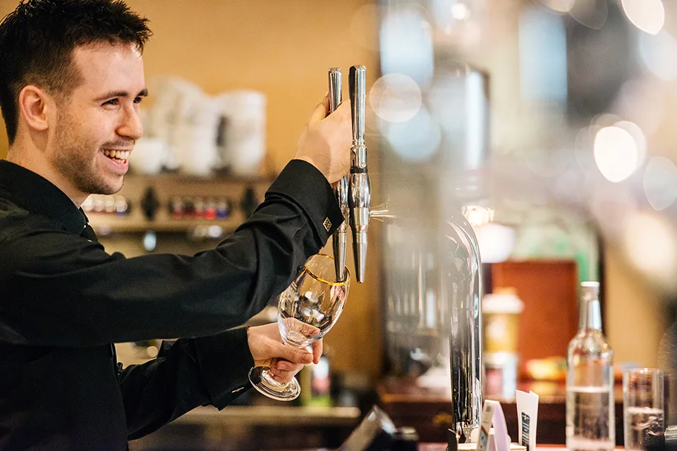 A team member at the bar, smiling while pouring a pint. 